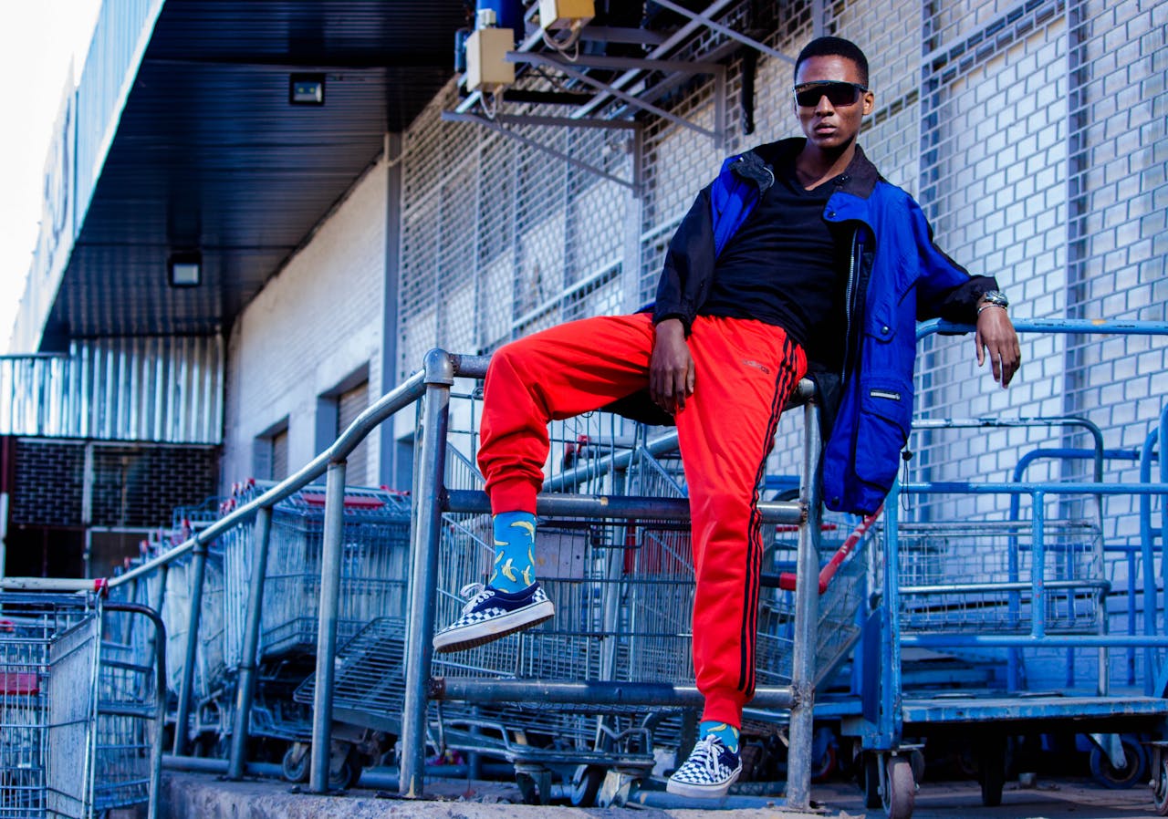 Street fashion portrait of a man sitting on a railing with a backdrop of shopping carts.